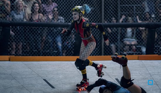 Harley Quinn op rolschaatsen tijdens een wedstrijd, draagt een rood en zwart pak met visnetkousen.