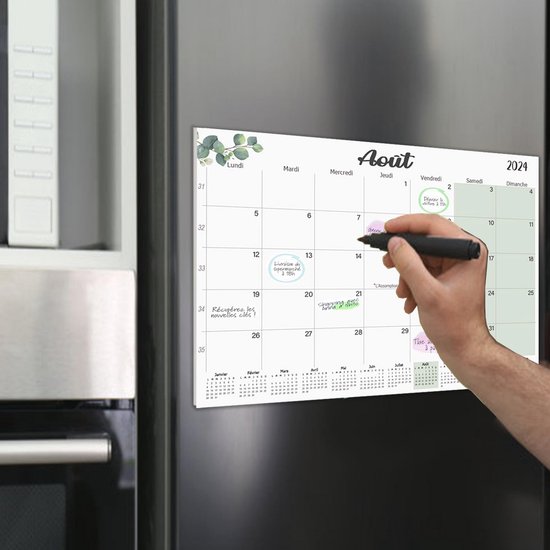 Magnetische koelkastkalender 2025 met groene bladeren en de maand "Février", getoond op een koelkast met een hand die schrijft.