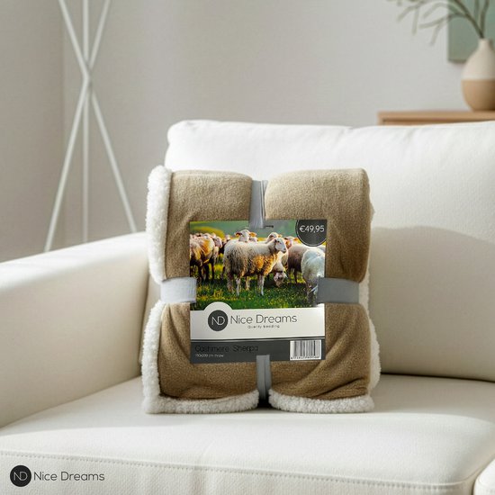 Een taupe plaid met witte sherpa voering, verpakt met een kaart met schapen. "€49,95" en "Cashmere Sherpa 150x200 cm" zichtbaar.