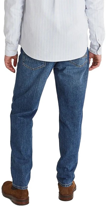 Model met spijkerbroek met taps toelopende pijpen, achterkant zichtbaar, in middelblauwe denim met licht waseffect.