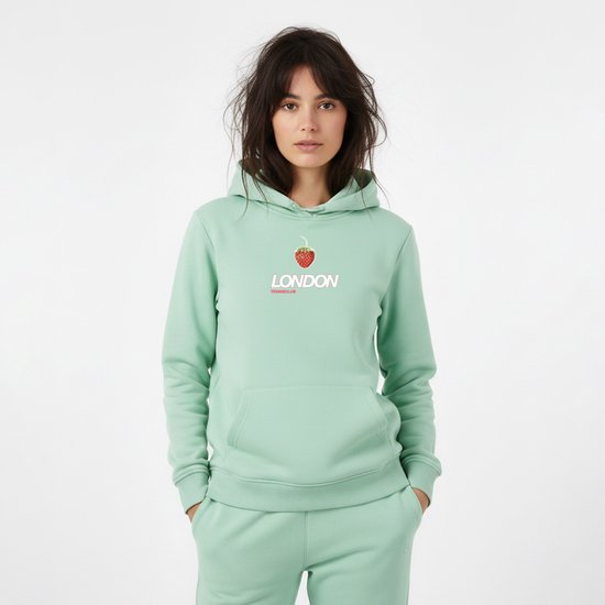 Een lichtgroene hoodie gedragen door een vrouw, met op de voorkant een print van een aardbei en de tekst "LONDON TENNISCLUB".