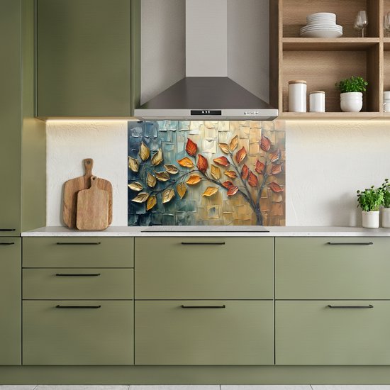 Keukenspatscherm met abstracte boom, gouden en oranje bladeren, boven een inductiekookplaat. Moderne groene keukenkasten.