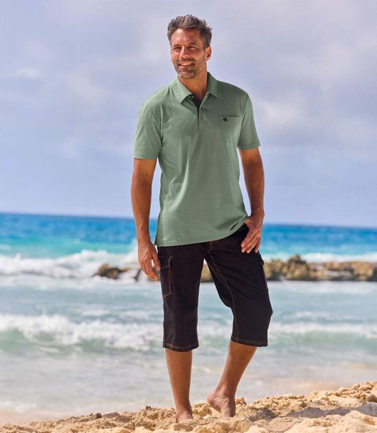 Man met lichtgroene polo met korte mouwen en borstzak met zwarte plantenprint, op strand.