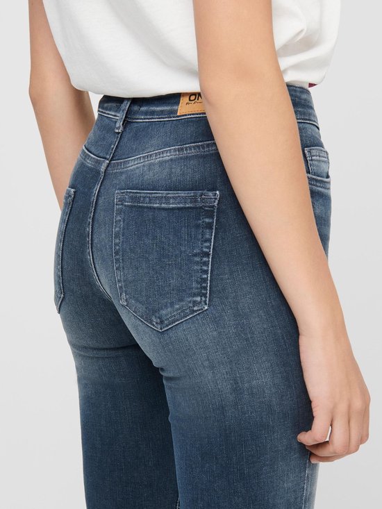 Gedetailleerde achterkant van een blauwe skinny jeans met rafels aan de zoom.