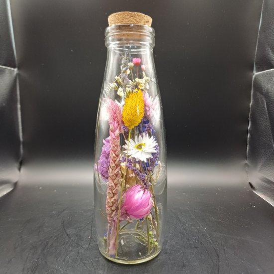Glazen fles met kurk, gevuld met gedroogde bloemen in roze, paars, geel en wit.