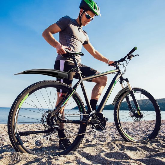 Man met fiets op het strand, met zwarte spatborden met groene accenten, zonnebril en helm.