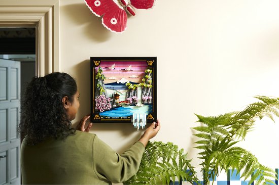 Een vrouw hangt een LEGO Art Japanse Kersenbloesem Landschap muurdecoratie op aan de muur.