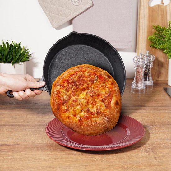 Hand die een zwarte gietijzeren koekenpan met pizza vasthoudt.