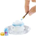 Een hand gebruikt een kwast om blauw glinsterend poeder op een witte miniatuur theepot te doen.