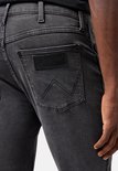 Close-up van de achterzak van een grijze spijkerbroek met een zwart Wrangler logo-patch.