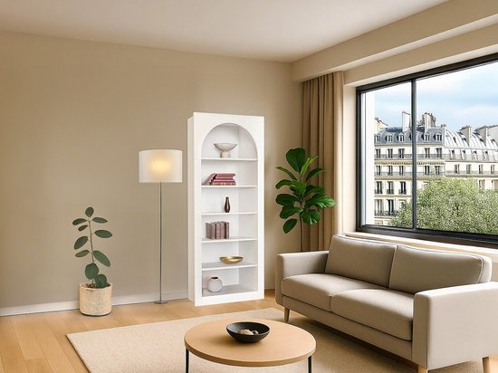 Witte boekenkast met ronde boog bovenaan, gevuld met boeken en decoraties, in een woonkamer bij een raam.