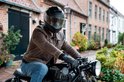 Man op een motor met een matzwarte systeemhelm en bruine leren jas.