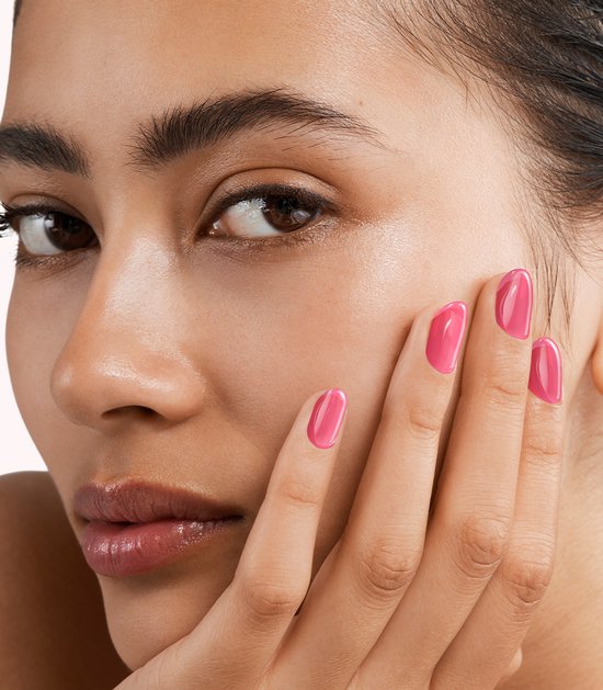 Close-up van een vrouw die haar gezicht aanraakt met een hand met gelakte nagels in een roze kleur.