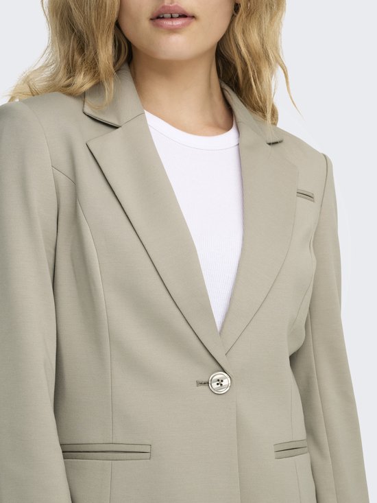 Lichtbeige blazer met één knoop en een witte top. De blazer heeft twee klepzakken.