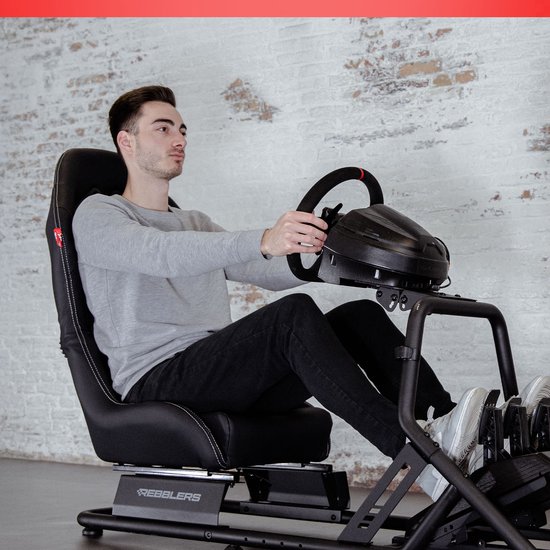 Man in grijze trui en zwarte jeans racet in een zwarte kuipstoel met racestuur en pedalen.