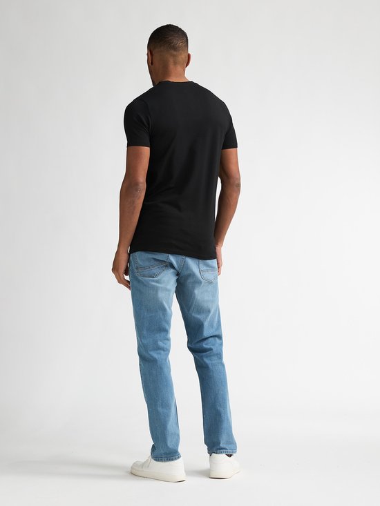 Man met donkere huid, draagt een zwart V-hals T-shirt en lichtblauwe jeans, gezien vanaf de achterkant.