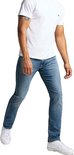 Man in een wit T-shirt en spijkerbroek loopt, met witte sneakers. De spijkerbroek is lichtblauw en slank.
