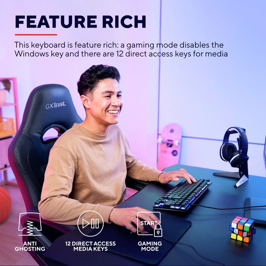 Man die lachend gamet op een zwart GXT Trust toetsenbord met meerkleurige verlichting, zittend in een gamestoel.
