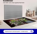 Een inductiebeschermer met een boeket bloemen, staande op een aanrecht naast een grijze spatscherm.