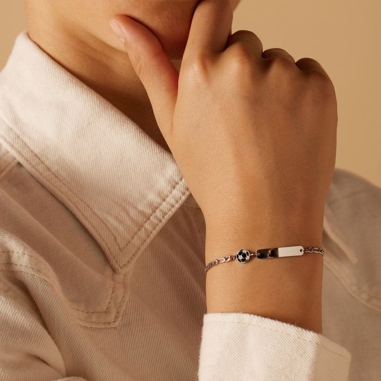 Zilverkleurige armband met figaro schakels, een voetbalbedel en een glad plaatje, gedragen om een pols.