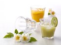 Deux verres, l'un avec un cocktail au kiwi et une tranche de kiwi, l'autre avec du jus d'orange et des tranches d'orange, avec des fleurs blanches.