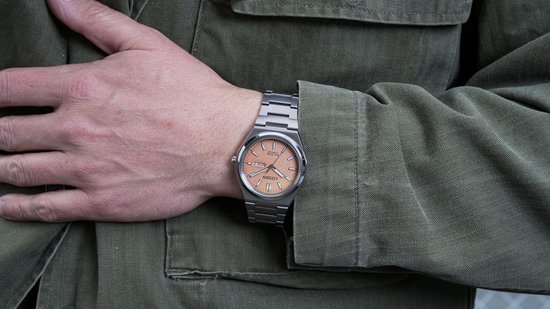 Citizen Eco-Drive horloge met perzikkleurige wijzerplaat, gedragen op een mannelijke pols.