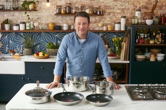 Jamie Oliver staat in een keuken met een set kookgerei, waaronder pannen en koekenpannen.