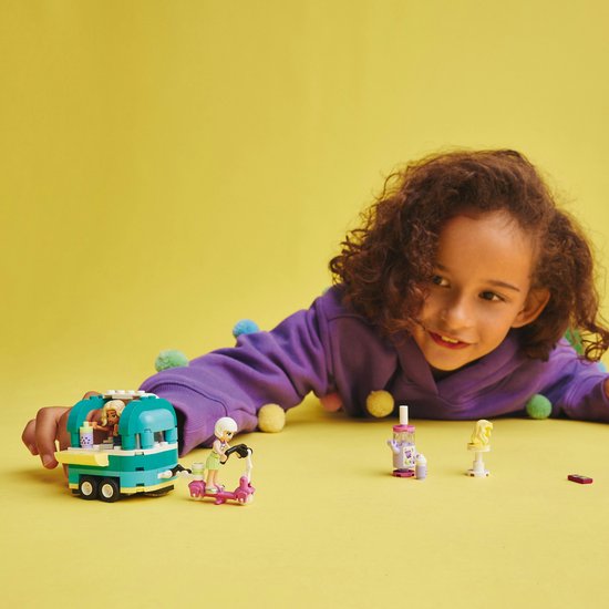 Kind met LEGO Friends bubbelthee kar, scooter en figuurtjes op gele achtergrond.