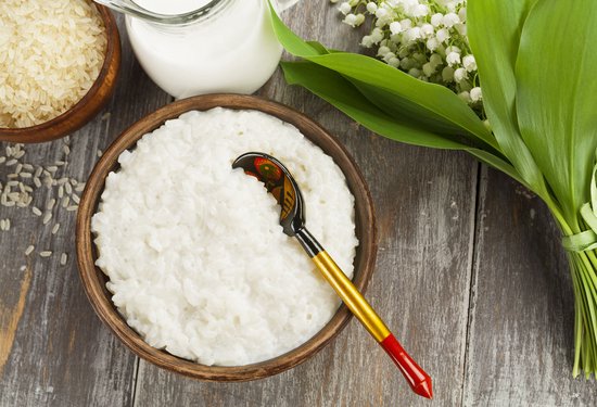 Houten kom gevuld met rijstepap, een houten lepel met traditionele decoratie, en een kannetje melk.