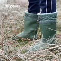 Dichtbij van groene winterlaarzen met witte fluffy voering, omringd door droge grasstengels.