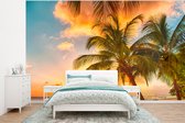 Behang - Fotobehang Zonsondergang - Palmboom - Wolken - Zee - Strand - Breedte 320 cm x hoogte 240 cm