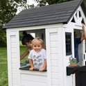 Kinderen spelen in een wit speelhuisje. Een jongen in een t-shirt met auto's kijkt naar buiten.