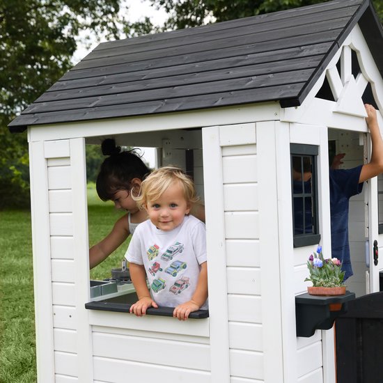 Kinderen spelen in een wit speelhuisje. Een jongen in een t-shirt met auto's kijkt naar buiten.