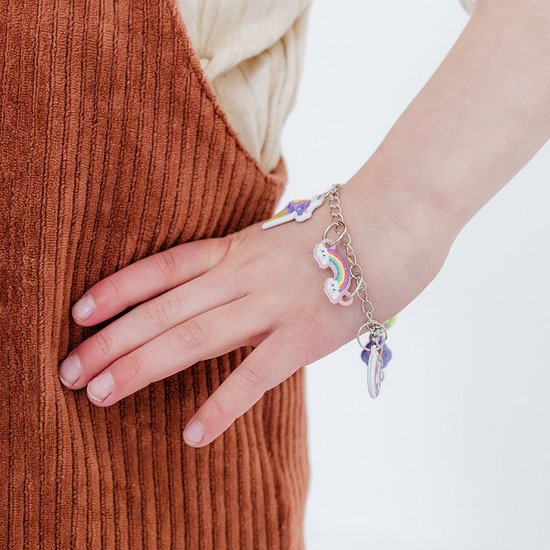 Arm van een kind dat een zilveren bedelarmband met eenhoorns, regenbogen en ijsjes draagt.
