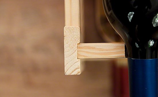 Houten wijnrek met zichtbare houtnerven, een fles met blauwe dop erop geplaatst.
