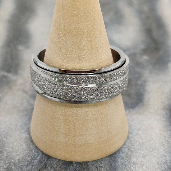 Zilverkleurige ring met een glinsterende, gestreepte band in het midden, op een houten standaard.