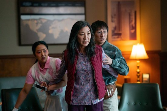 Michelle Yeoh met een derde oog op haar voorhoofd en rood gilet, met twee andere personen in paniek.