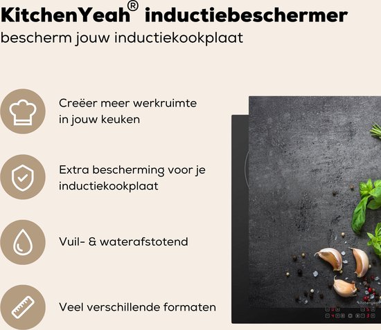 Zwarte inductiebeschermer met betonprint, bedekt met kruiden, knoflook, citroen en peperkorrels.