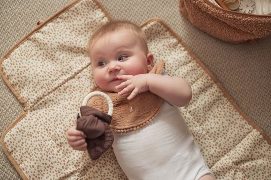 Baby met slabbetje en bijtring op een crèmekleurige verschoningsmat met dierenprint.