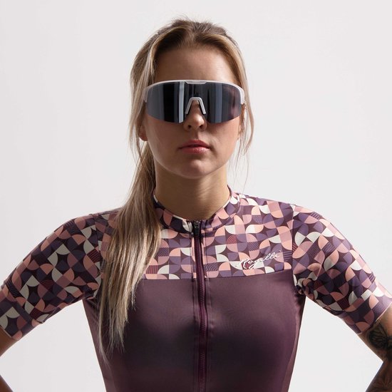 Vrouw met blonde paardenstaart draagt een wielrenshirt met geometrisch patroon en witte zonnebril.