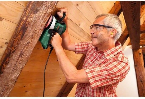 Man met veiligheidsbril schuurt een houten plafond.
