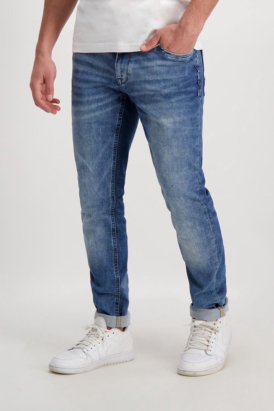 Man in blauwe slim fit jeans met lichte wassing en opgerolde zoom, met witte sneakers.