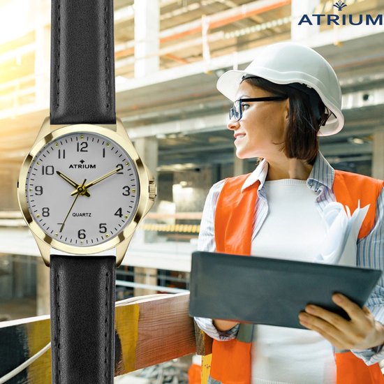 Montre dorée avec cadran blanc et bracelet noir, portée par une femme casquée sur un chantier.