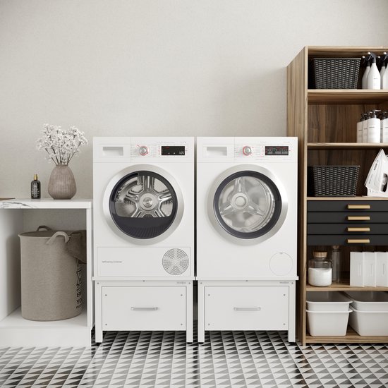 Twee witte wasmachines op ladekasten, in een wasruimte met een houten kast, een mand en betegelde vloer.