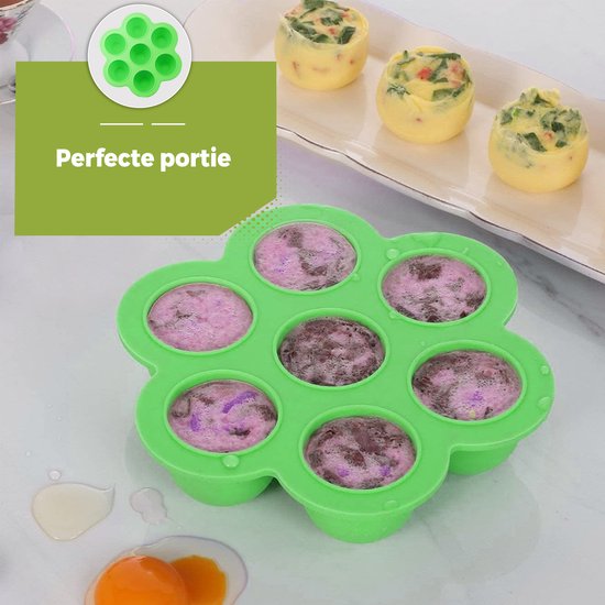 Lichtgroene siliconen bakjes in bloemvorm, gevuld met roze en bruine babyvoeding. Gebakken eitjes op de achtergrond.