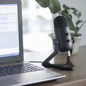 Fifine K678 USB microfoon op een zwarte standaard naast een laptop.
