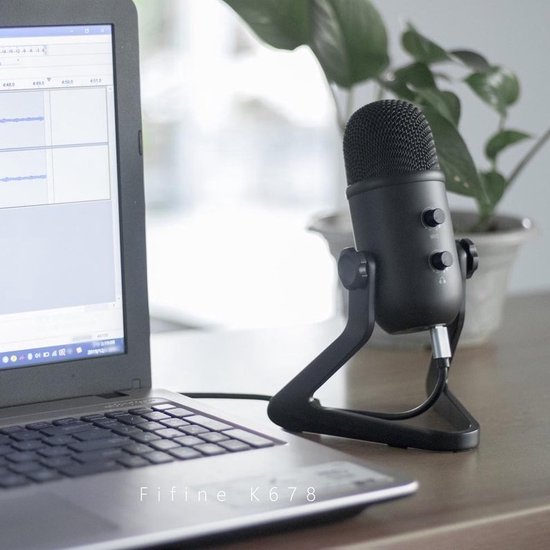 Fifine K678 USB microfoon op een zwarte standaard naast een laptop.
