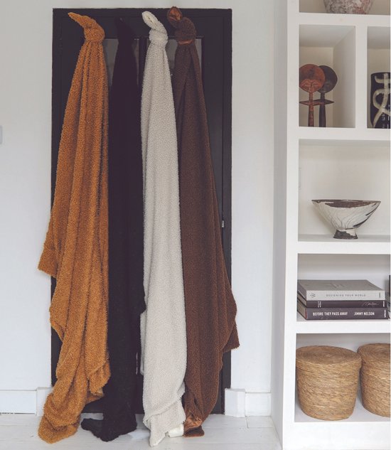Vier plaids, warmbruin, zwart, crème en donkerbruin, hangend aan haken.