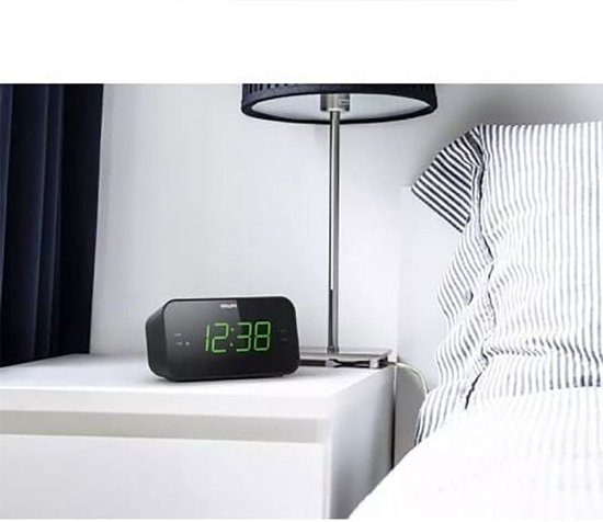 Zwarte Philips wekkerradio met groene digitale cijfers, op een nachtkastje naast een bed.