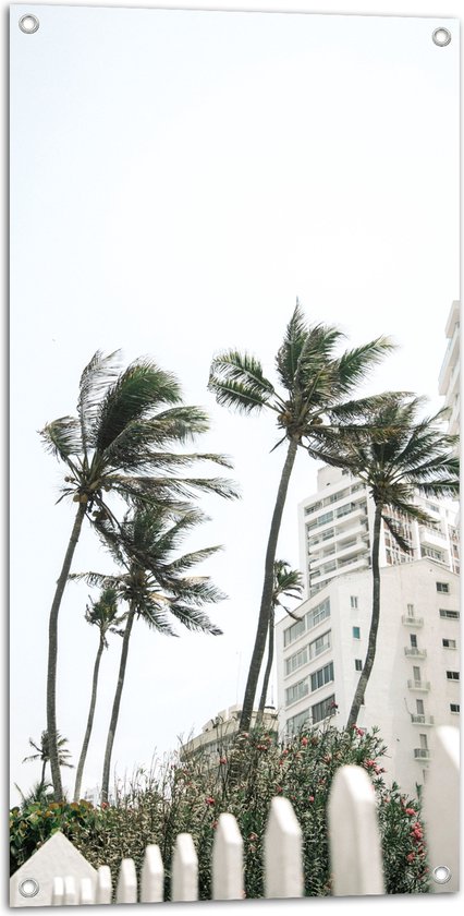 Tuinposter – Wind door Palmbomen bij Wit Gebouw - 50x100 cm Foto op Tuinposter (wanddecoratie voor buiten en binnen)